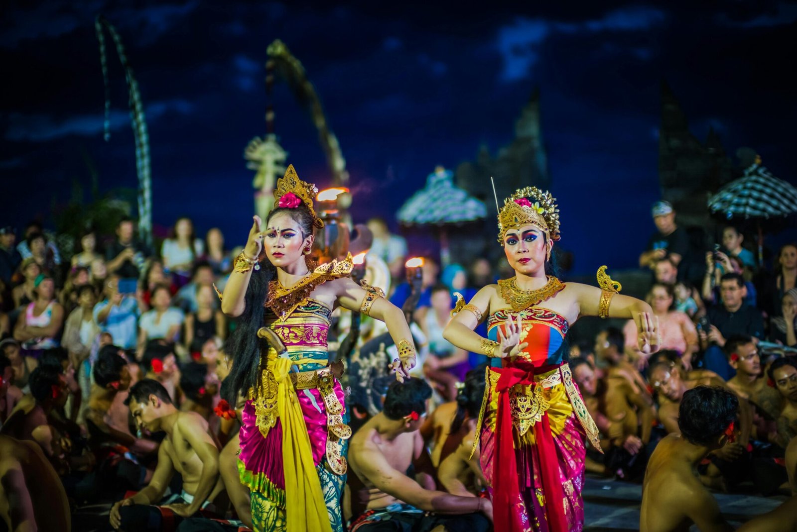 Two women perform traditional Balinese dance in colorful costumes during a festival.