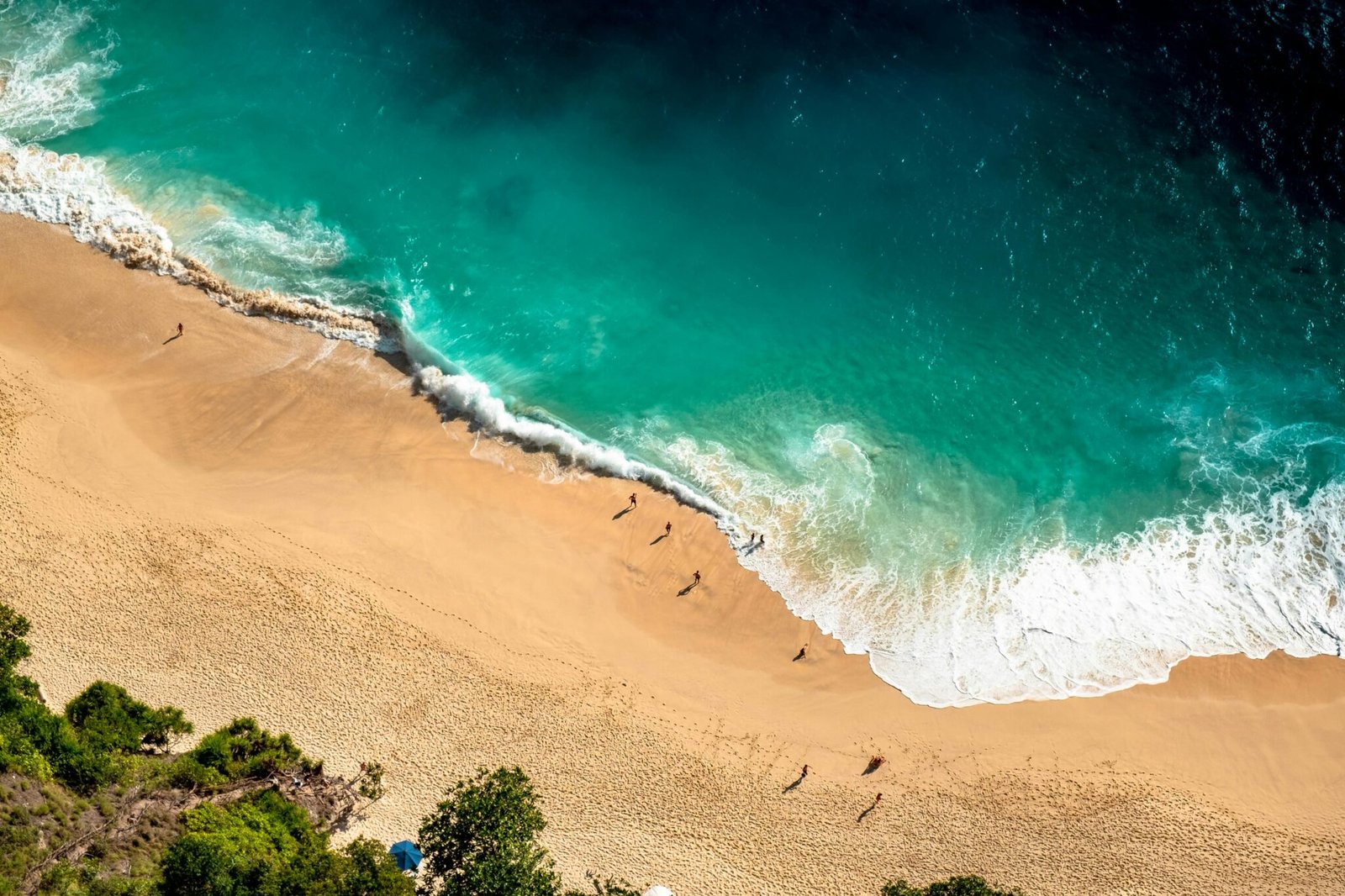 Stunning aerial view of Bali's beach with turquoise waves crashing on golden sand.